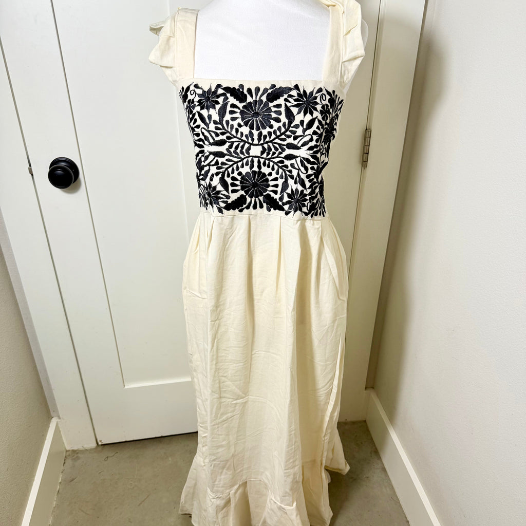 White dress with black floral pattern on a mannequin against a white wall.