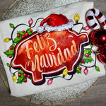 Load image into Gallery viewer, Tshirt with 'Feliz Navidad' text and Christmas elements on a wooden surface.
