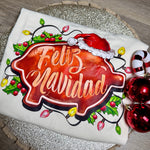Load image into Gallery viewer, Decorative tshirt with 'Feliz Navidad' text and Christmas elements on a wooden surface
